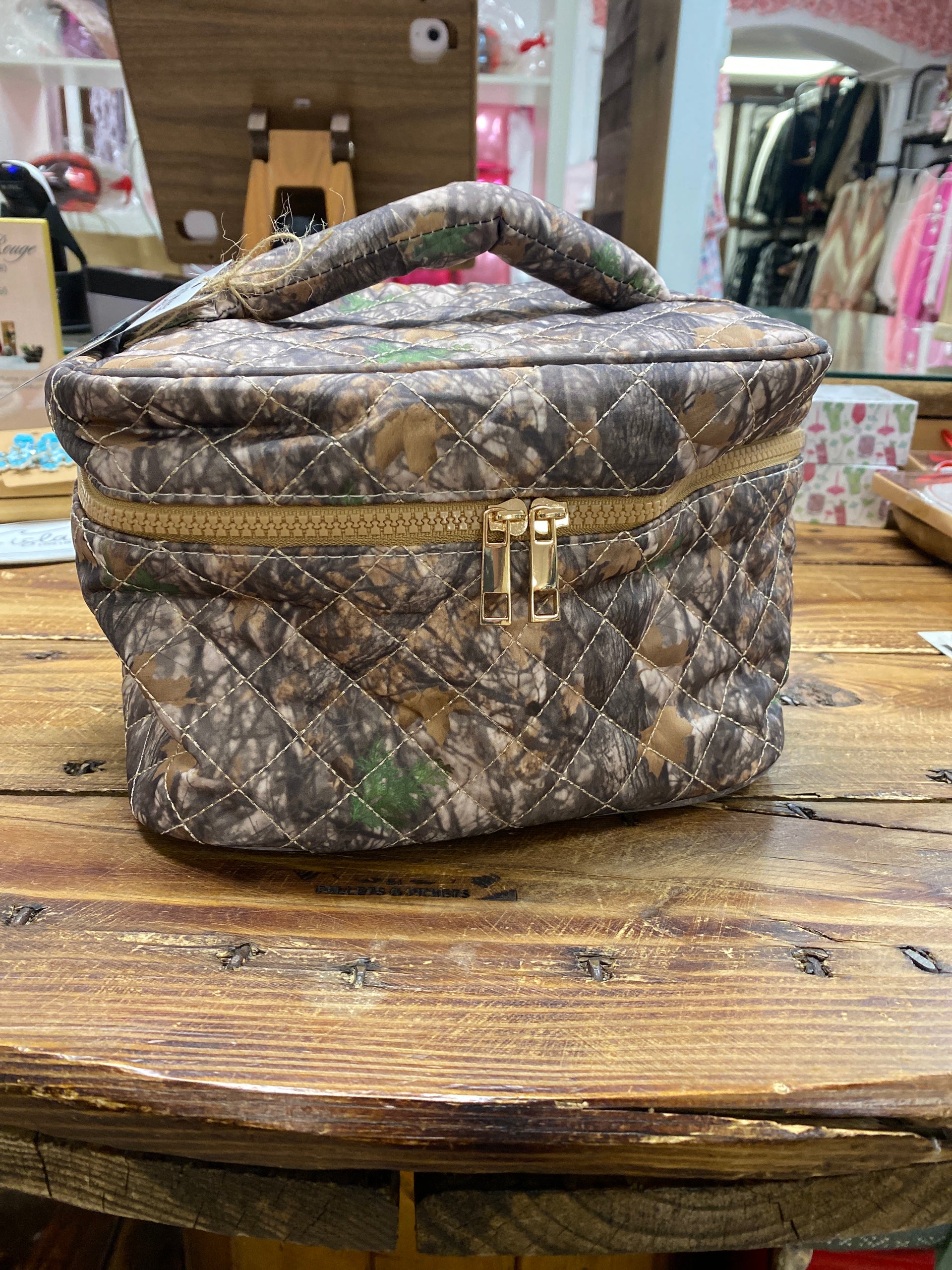Camouflage-patterned bag with gold zipper on a wooden surface