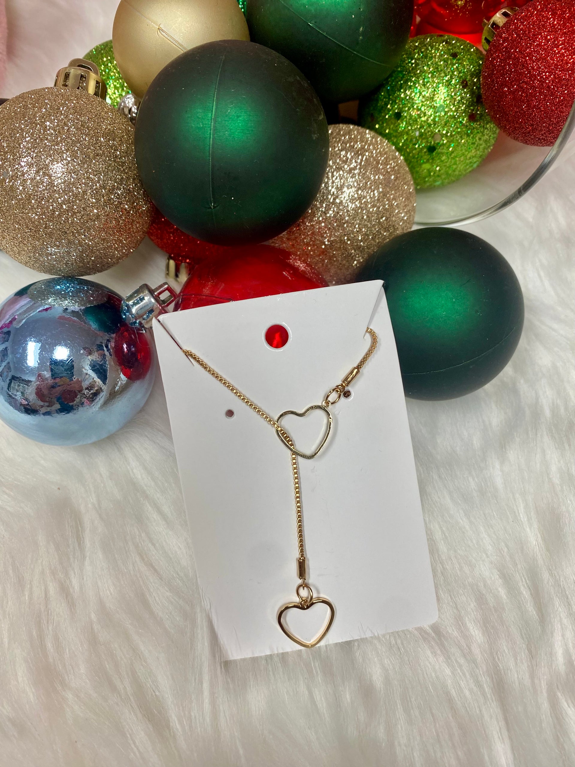 Gold necklace with heart pendants on a card in front of Christmas ornaments