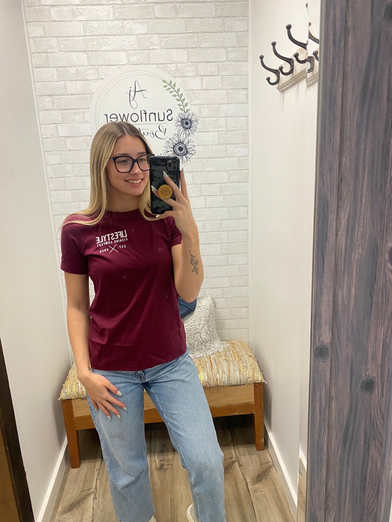Person wearing a maroon shirt with text, standing in a room with a wooden floor and white walls.